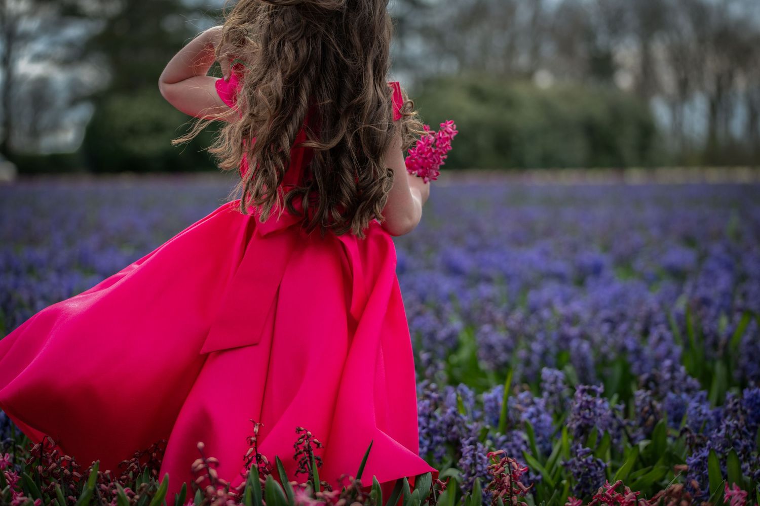 A flowing red dress twirls among a vibrant field of purple wildflowers on a spring day.