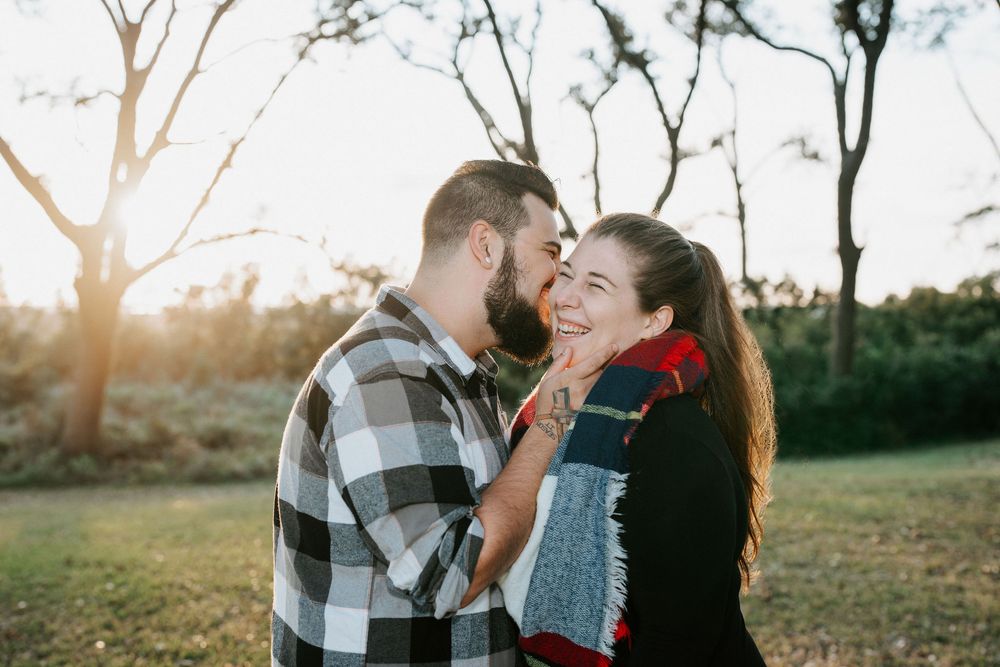 Couple embraces in a romantic outdoor setting during golden hour with sunlight streaming through trees.