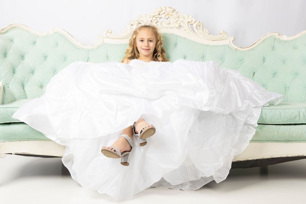 A fluffy white wedding dress train with lace details spreads across a light green couch or settee.