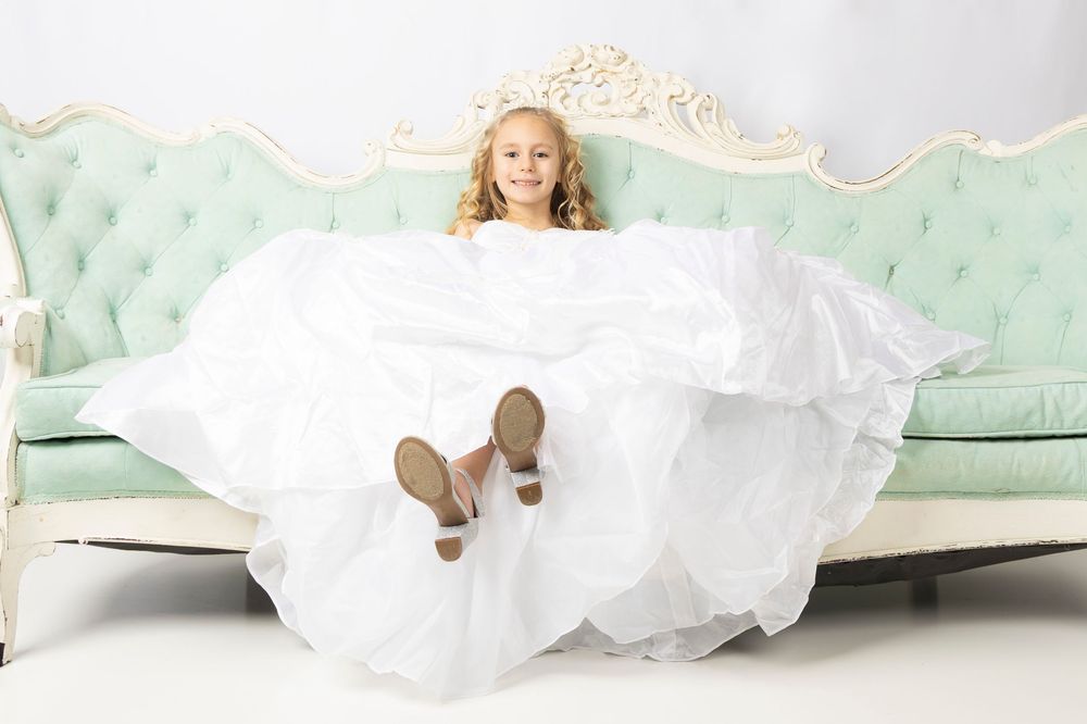 Child reclining on vintage-style mint green sofa wearing flowing white dress.