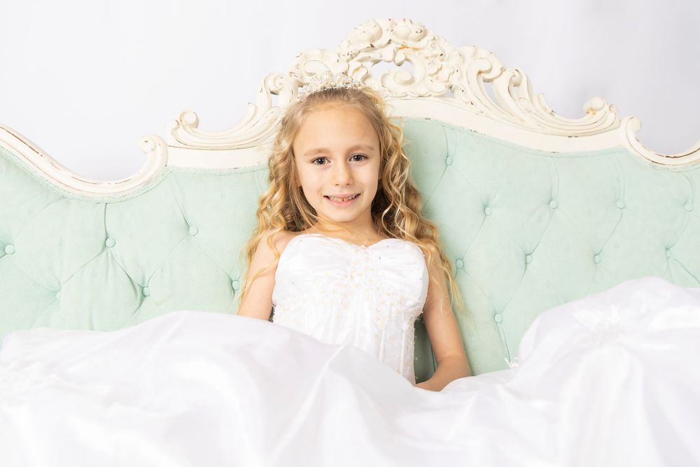 A young child in a white dress poses on a mint green backdrop with delicate floral decorations.