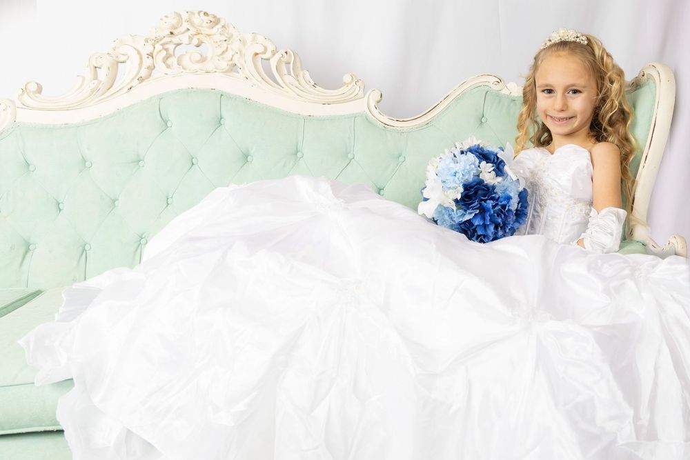 Young child in white dress laying on mint green tufted sofa with elegant decor.
