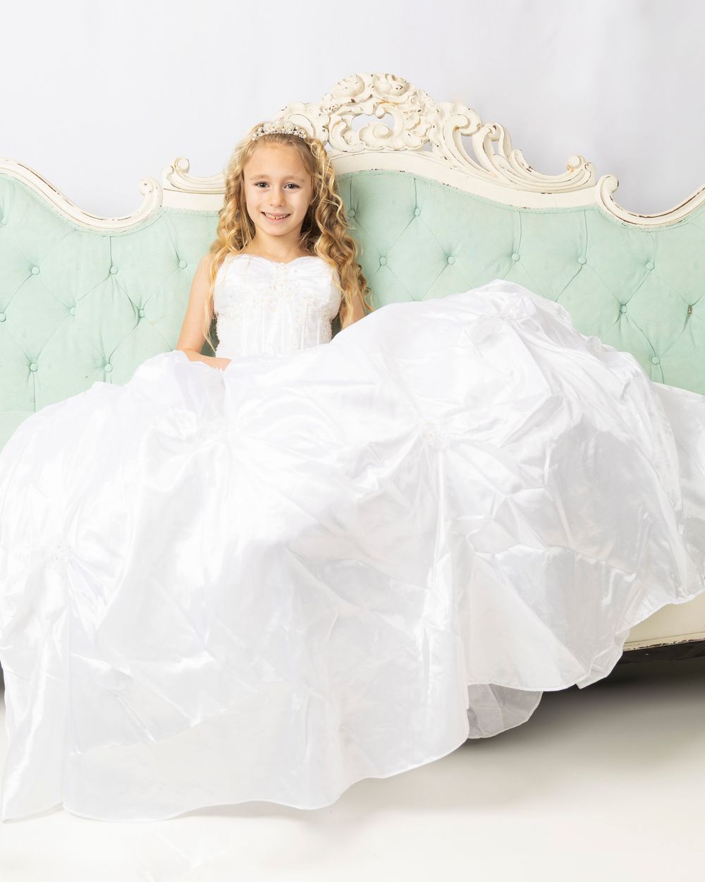 A person in a white flowing dress reclines gracefully on a mint green vintage sofa for a portrait session.