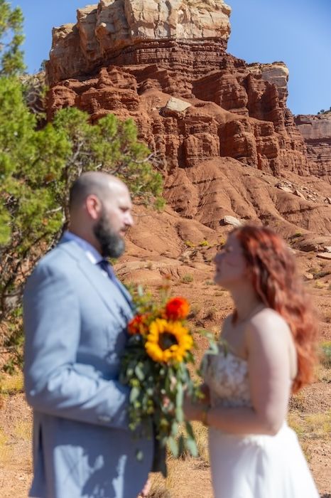 A couple shares a romantic moment during their wedding ceremony against stunning red rock formations in a desert landscape.