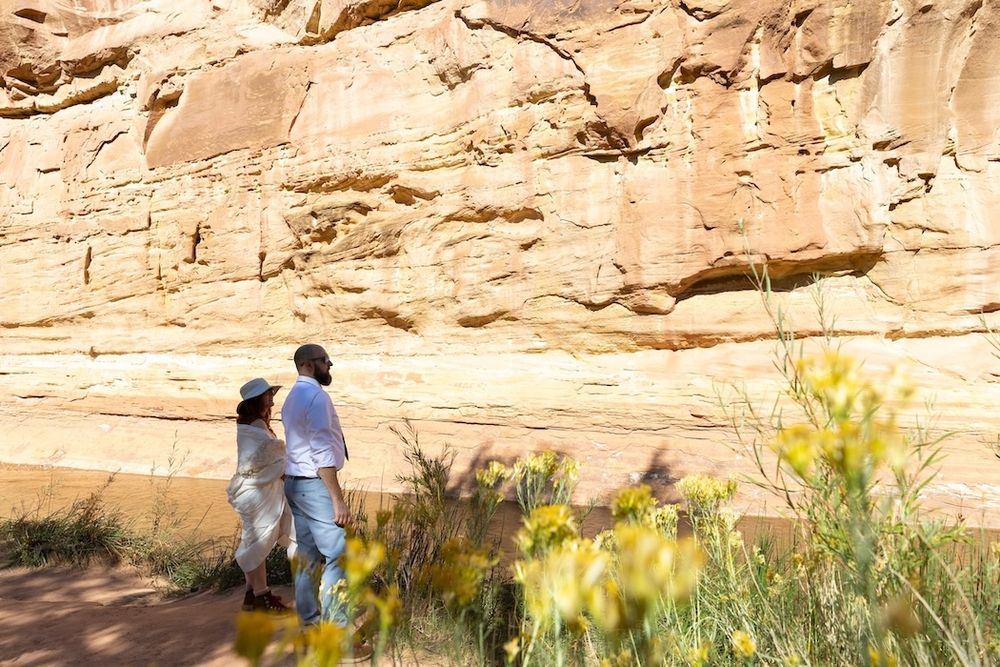 A group of hikers explore a scenic desert canyon trail with towering sandstone cliffs and green vegetation.
