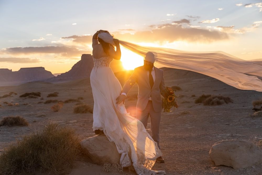A figure in white clothing walks through a desert landscape at sunset with dramatic clouds and sunlight.