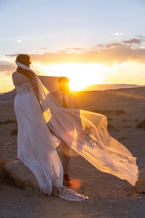 A figure in flowing white fabric dances against a desert sunset creating an ethereal silhouette effect.