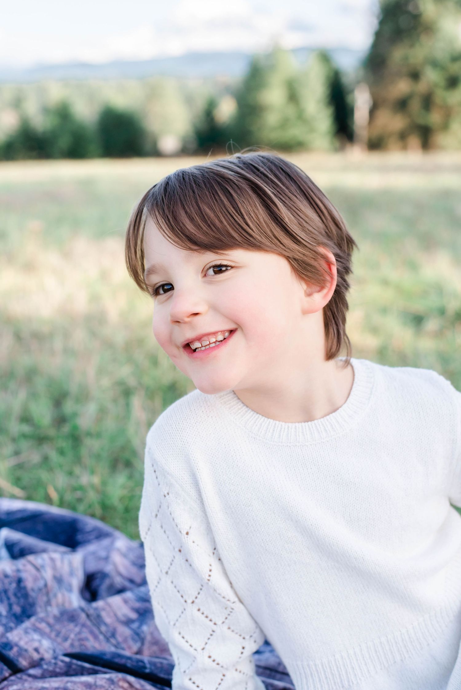 A series of four outdoor portrait photos showing a child wearing a white sweater against a natural background.