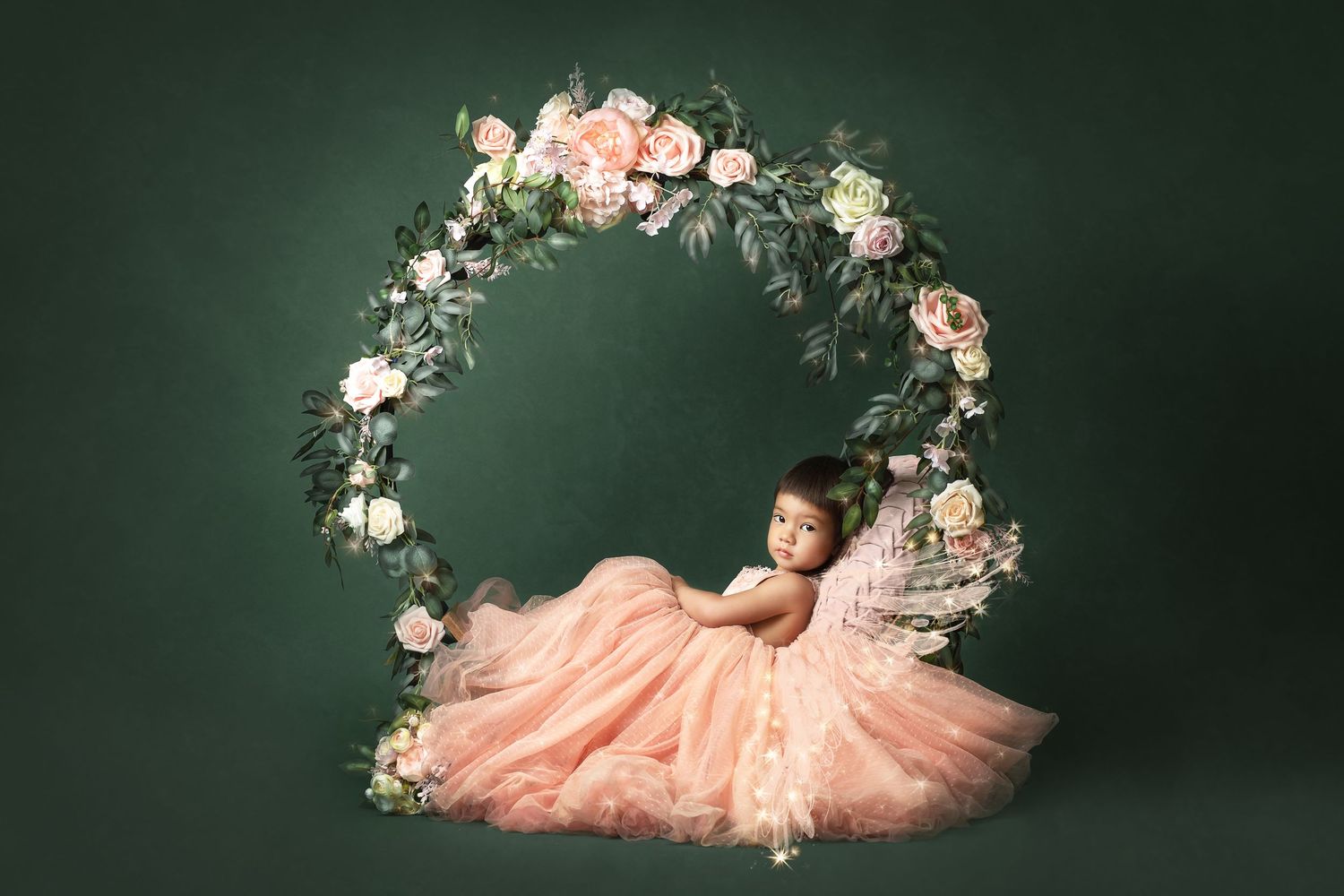 Pink tulle dress surrounded by delicate floral arrangements against dark green backdrop.