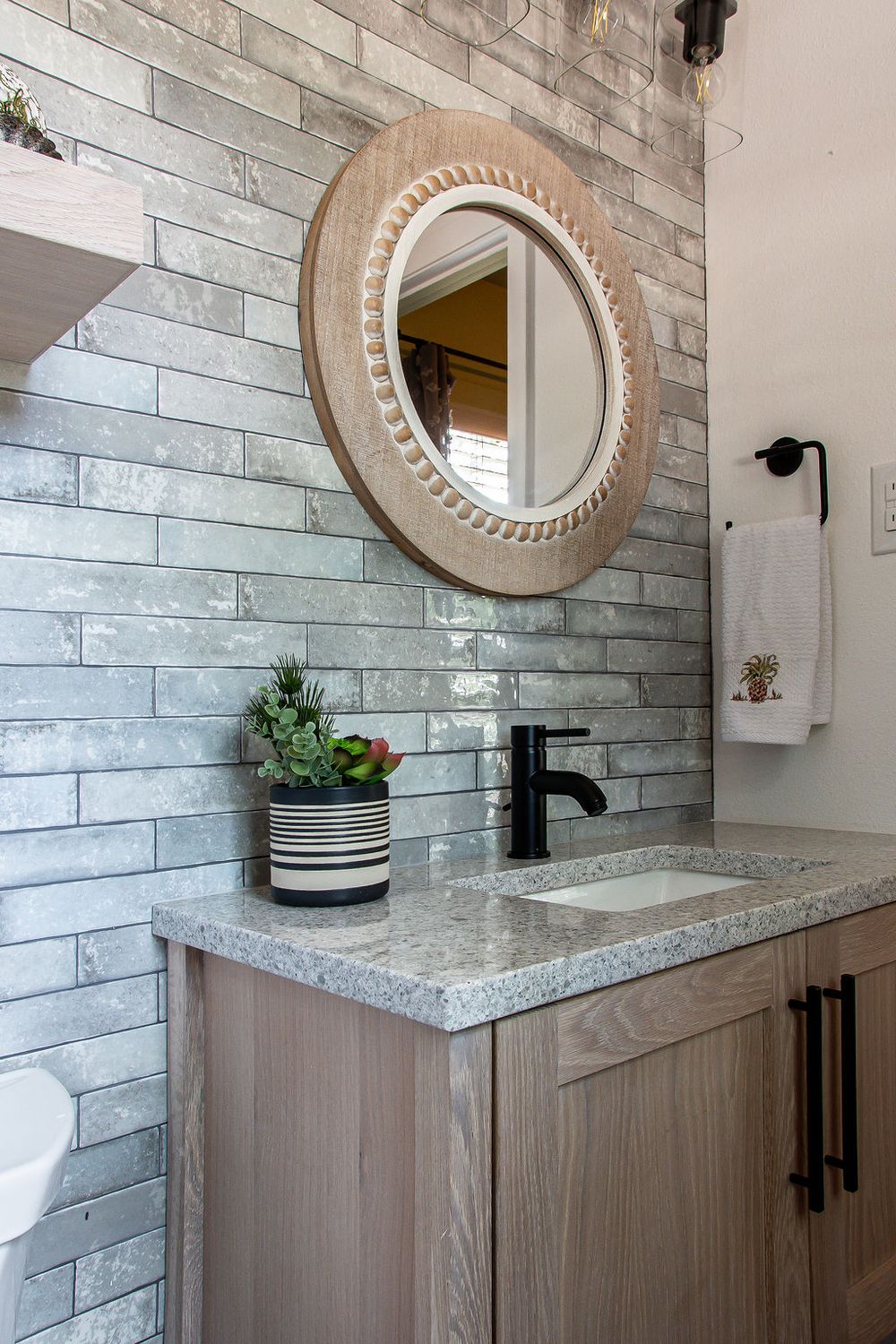 Rustic-modern bathroom design with a floor-to-ceiling stone accent wall and circular decorative mirror.