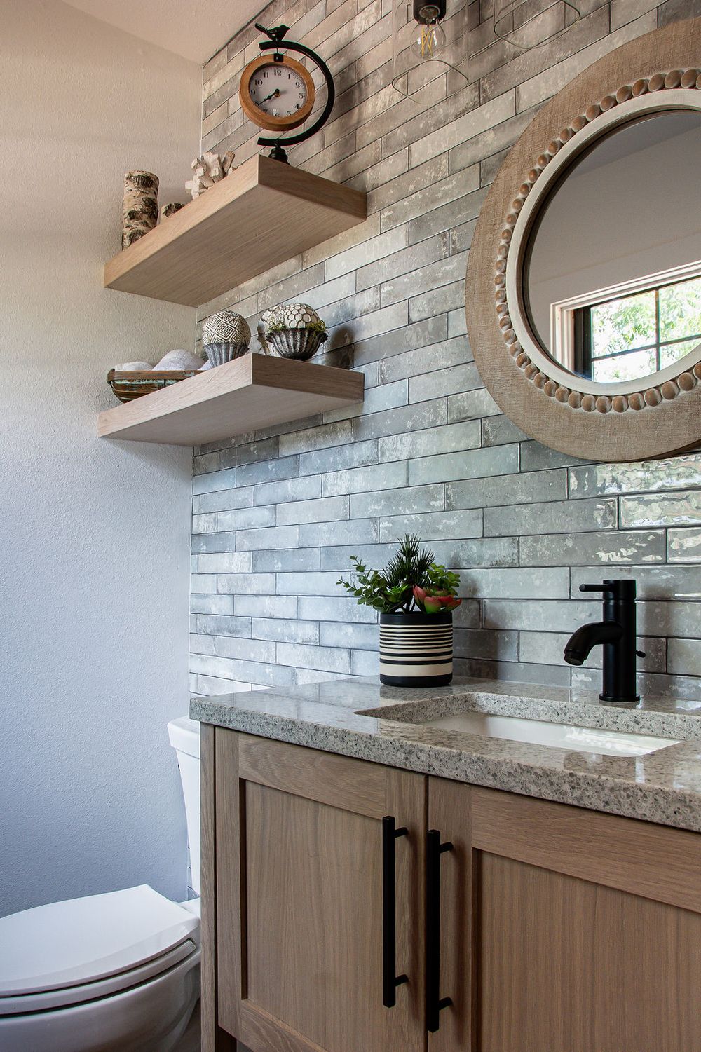Rustic-modern bathroom design with a floor-to-ceiling stone accent wall and circular decorative mirror.