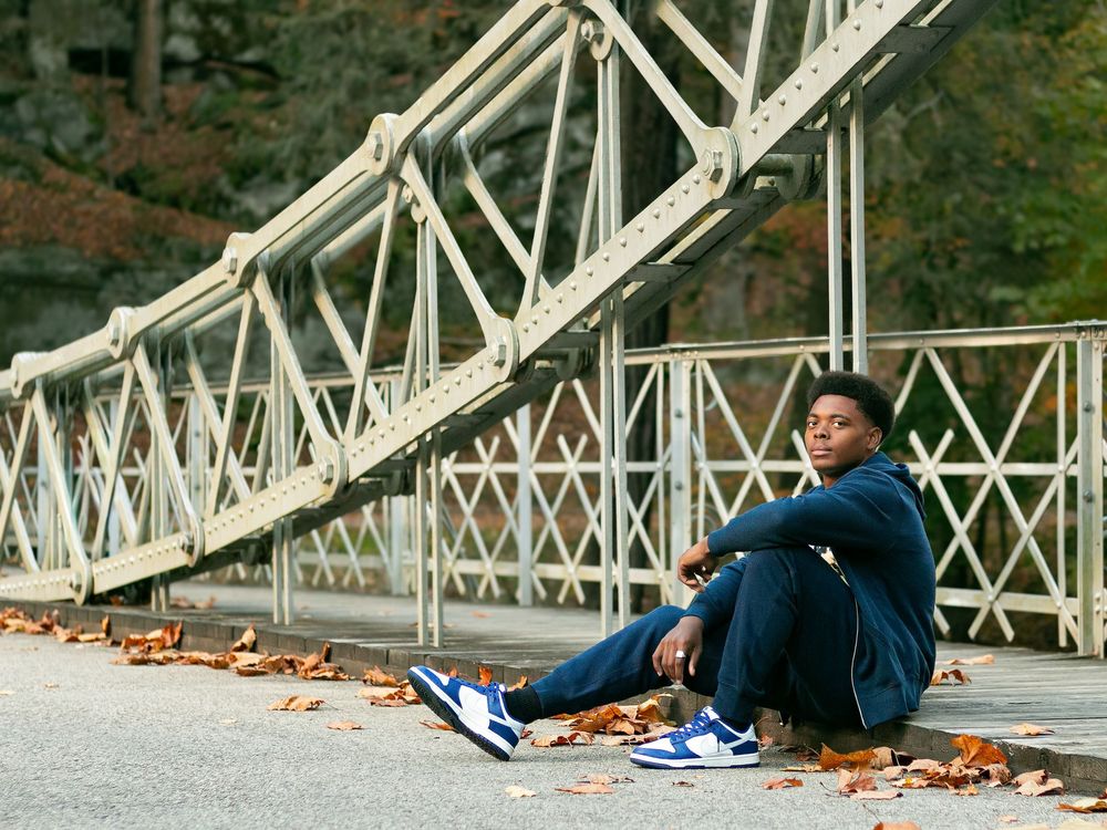 Someone sits on fallen autumn leaves beside a white metal bridge structure wearing blue clothing and sneakers.