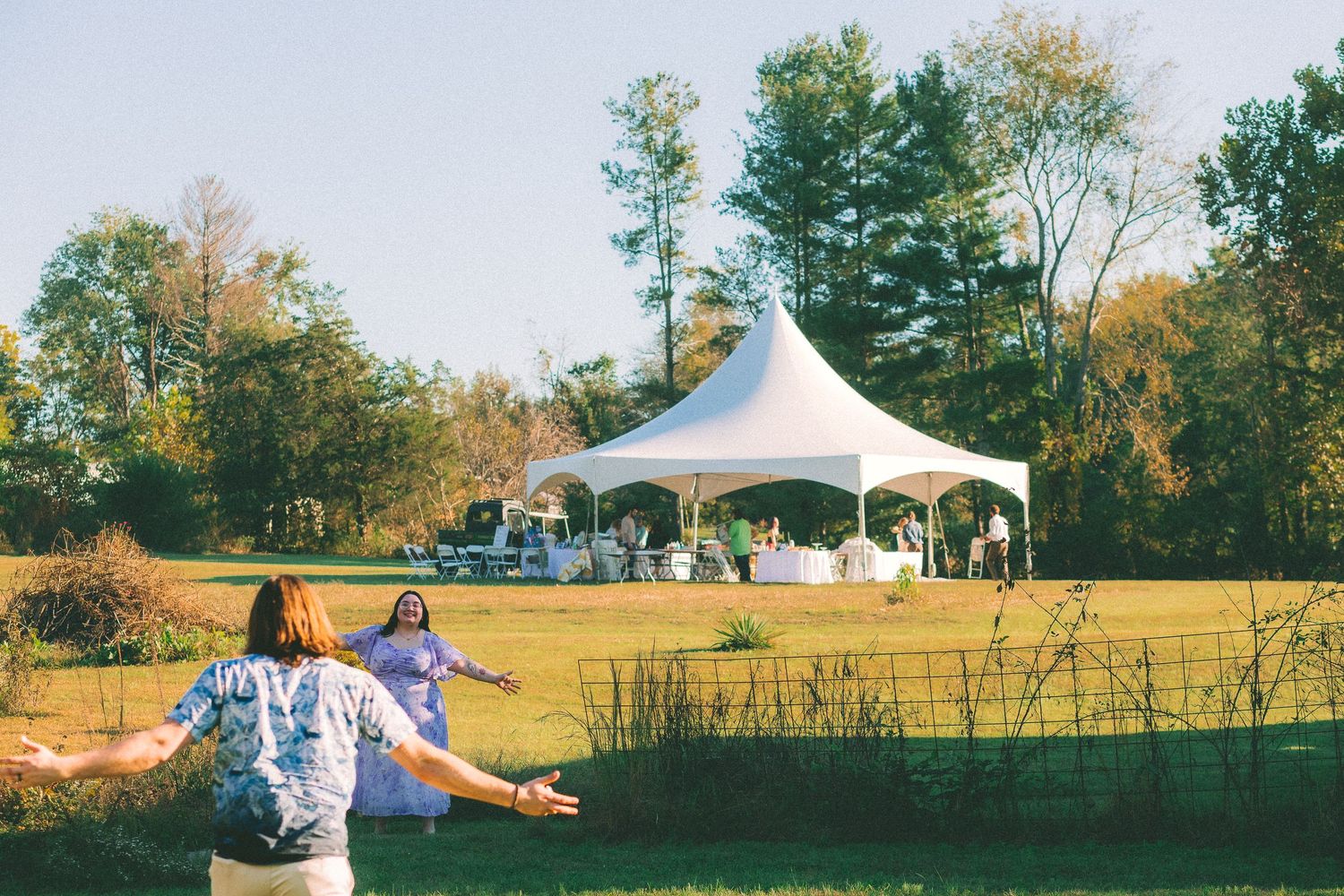 A panoramic view of a rural outdoor event with white tents and people gathered on a grassy hillside in autumn.