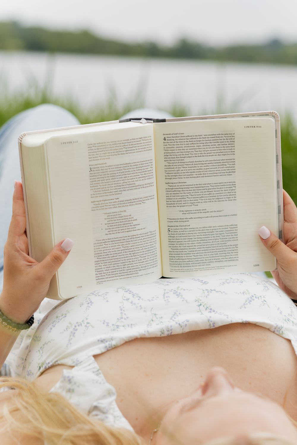 Person lying on white bedding while reading a book, creating a cozy and relaxed reading atmosphere.