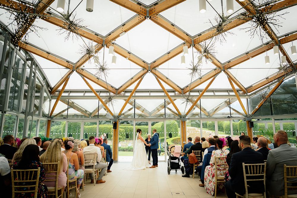 Wedding guests gather under a stunning glass conservatory ceiling with wooden beams during an elegant reception.