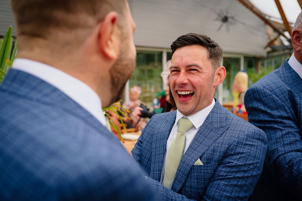 Groomsmen in navy checkered suits share a candid laugh during an outdoor wedding celebration.