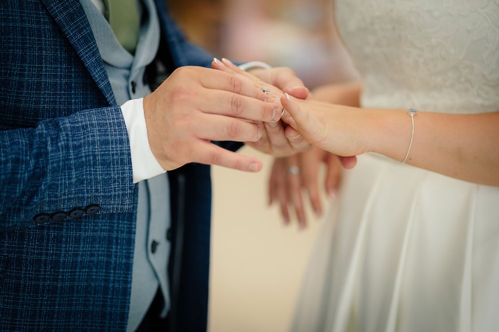 Close-up sequence of hands exchanging wedding rings during a traditional marriage ceremony.