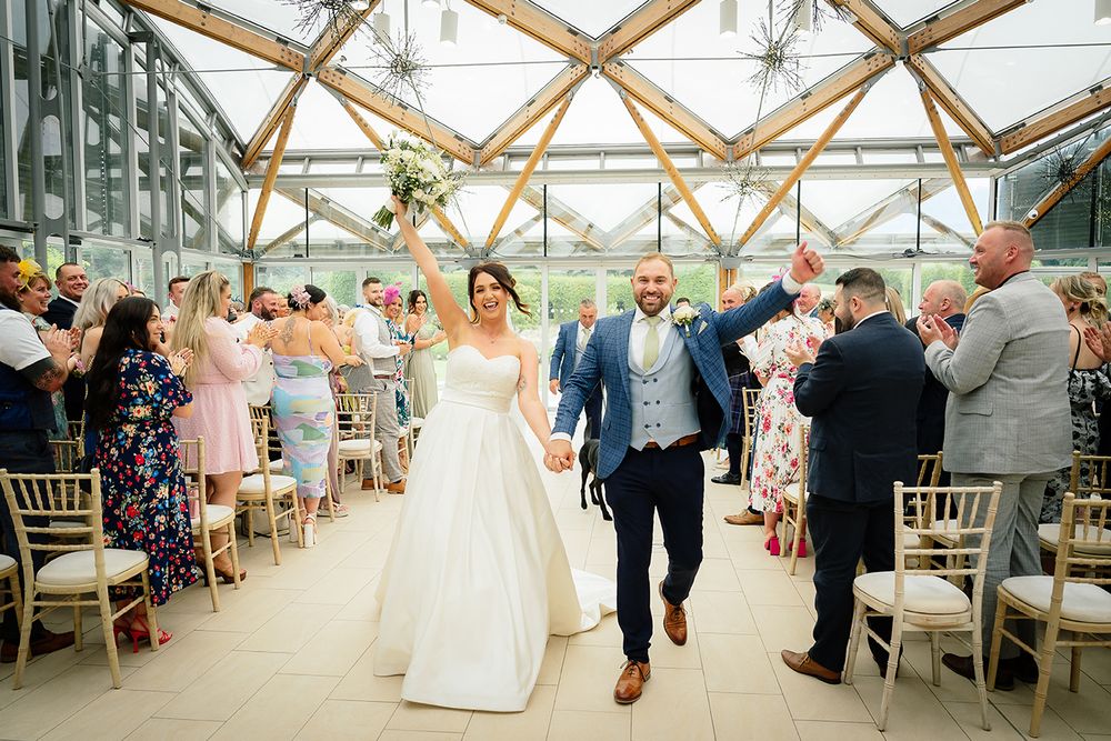 A wedding reception celebration in a bright glass conservatory with wooden beams and elegant table settings.