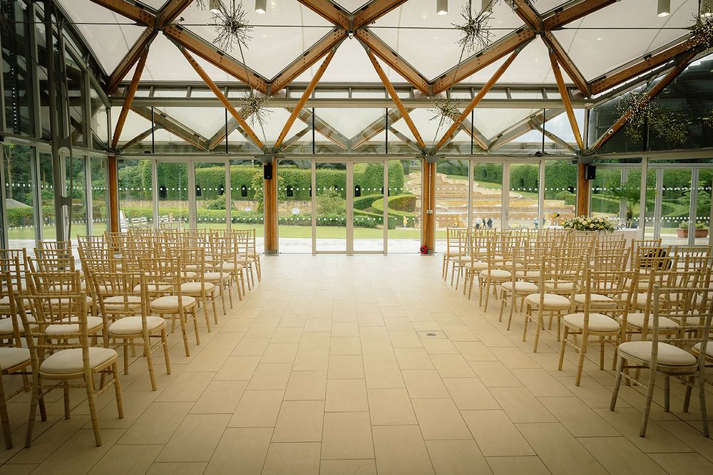 An elegant wedding ceremony setup with wooden chairs arranged in rows inside a rustic barn venue with natural lighting.