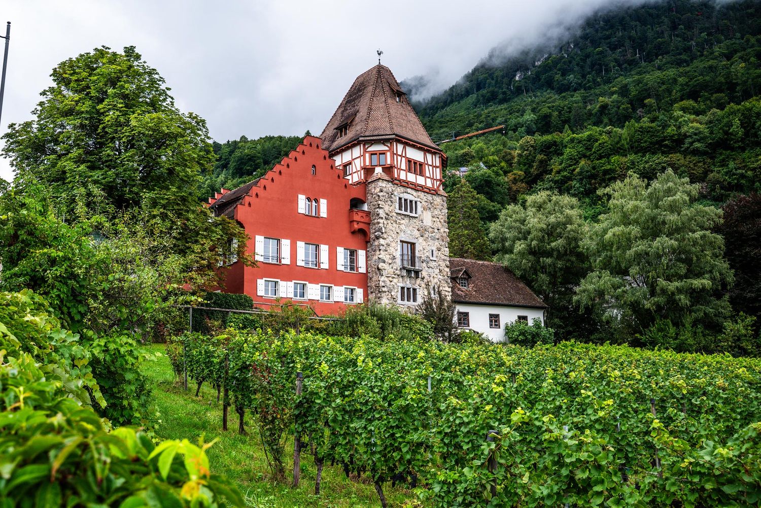 Scenic view of traditional houses nestled in lush green mountains with foggy peaks in the background.