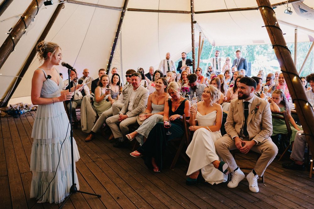 Wedding guests seated in rows under a large white tent during an outdoor ceremony.