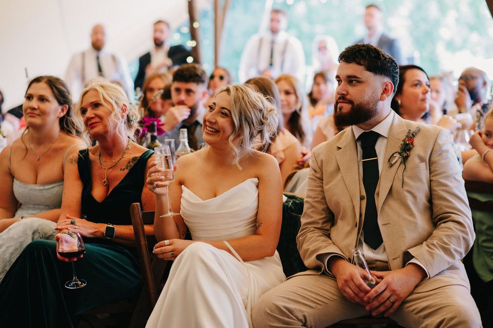 Wedding reception crowd laughing and enjoying speeches in a rustic tent venue.