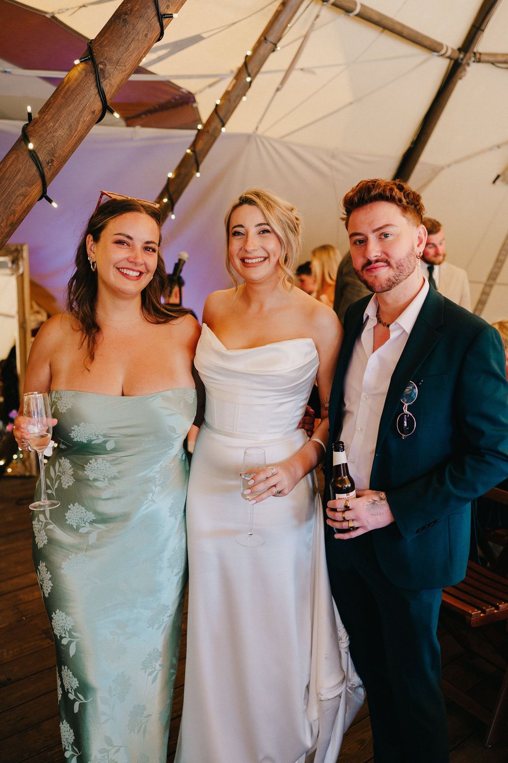 Wedding celebration under a tent with guests in formal attire including mint green and white dresses.