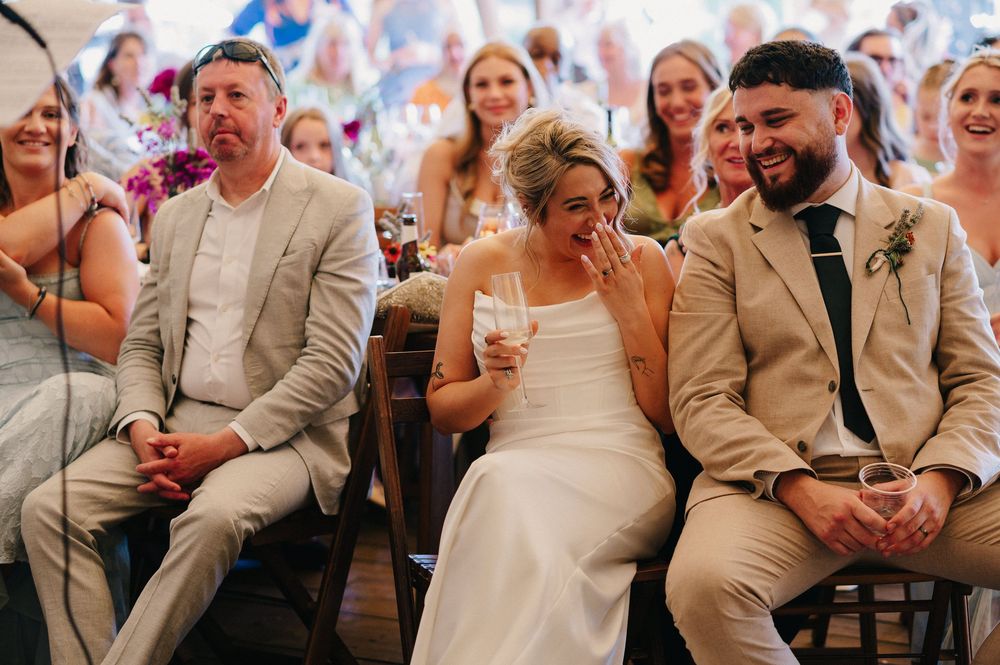 Wedding guests share joyful laughter while seated together at an outdoor celebration.