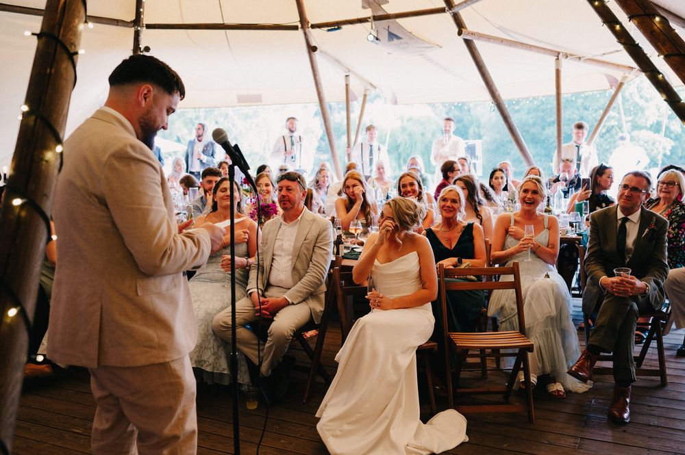 Wedding couple dances together during their first dance under a tent while guests watch and celebrate.