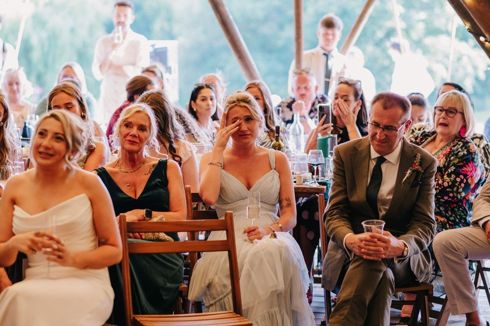 Guests share laughter and joy during wedding speeches inside a tent venue.