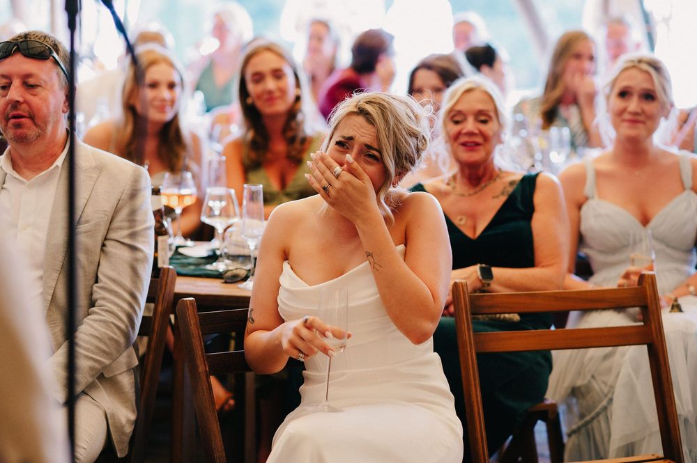 Wedding attendees react with emotion and laughter during reception speeches in a tent setting.