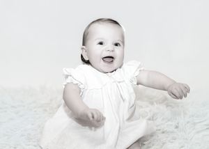 A series of black and white photos showing a baby's joyful expressions and movements while wearing white clothing.