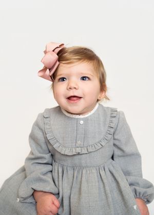 Baby wearing a gray ruffled dress with white trim poses against white background.