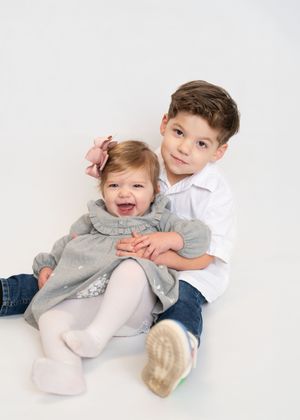 Three playful images of siblings in white and gray outfits showing joyful interaction on a light background.
