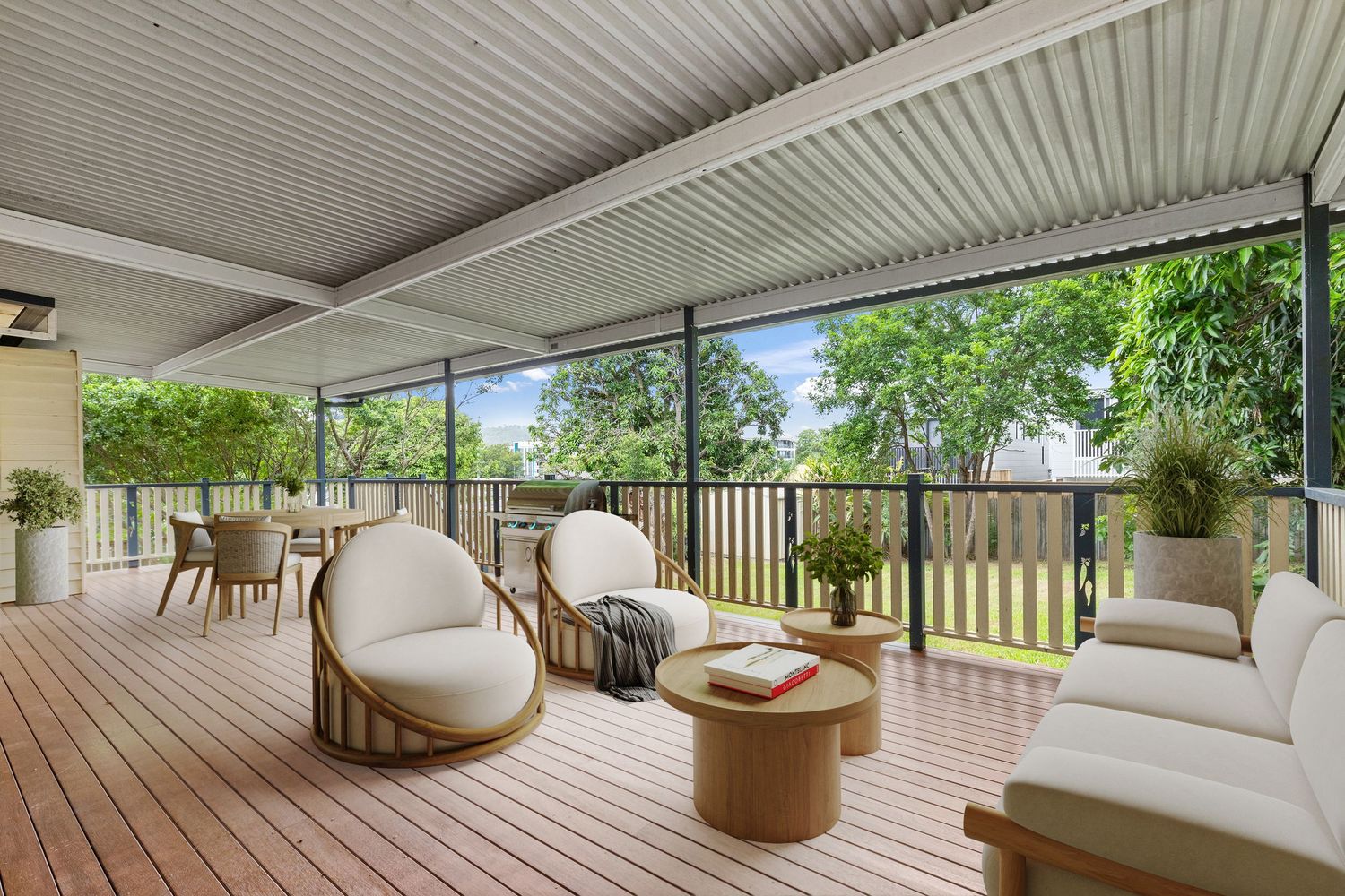 Spacious covered timber deck with white outdoor furniture, round coffee table, and leafy garden backdrop.