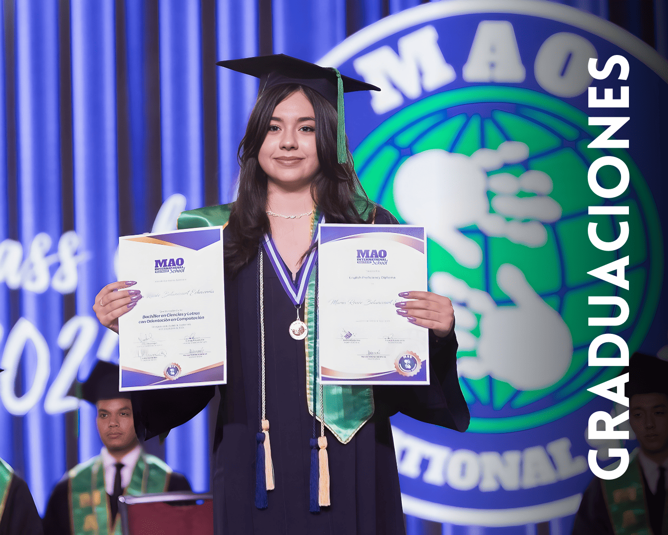 Graduates in dark robes hold up academic certificates during a graduation ceremony with blue lighting and green accents.