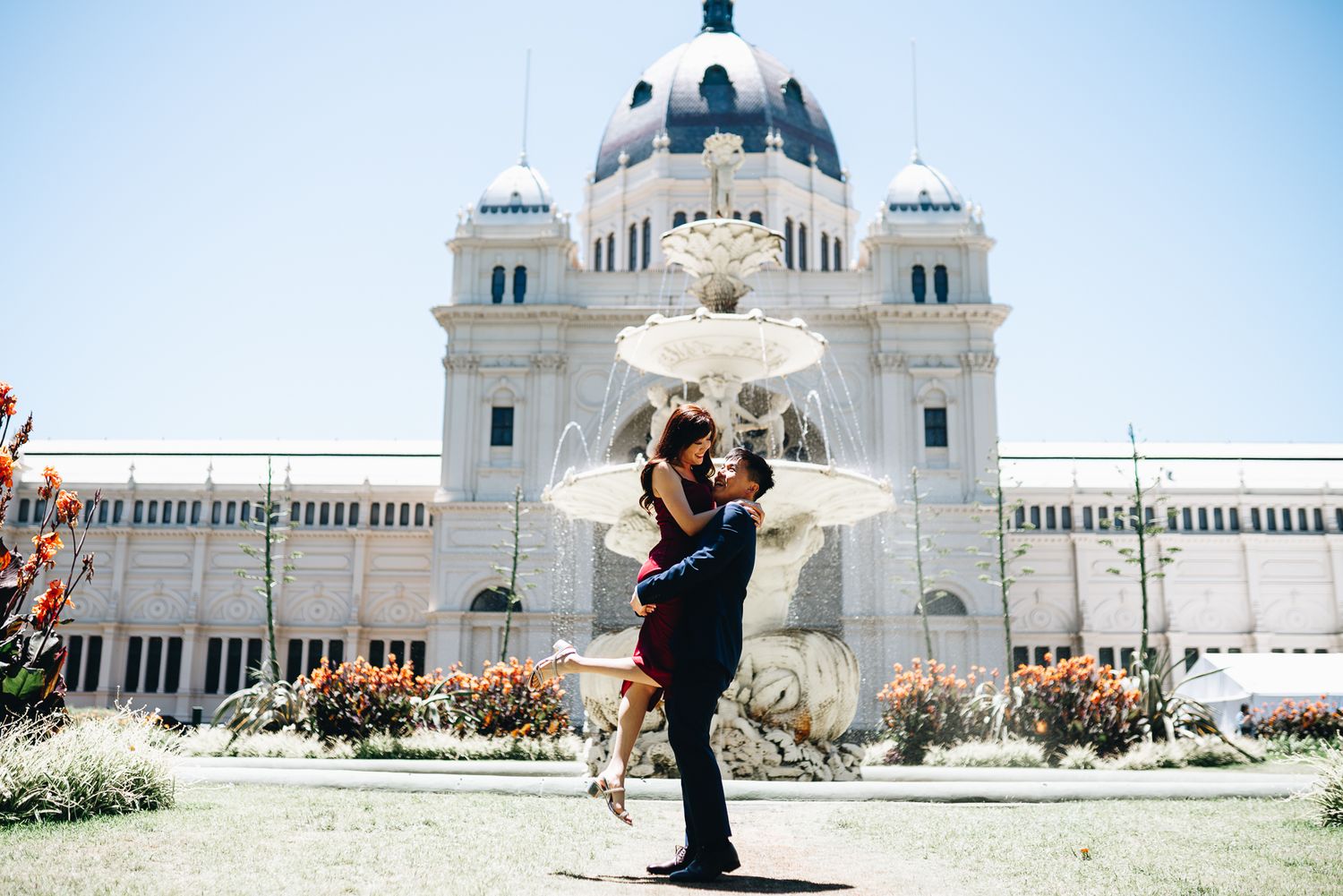 A man carrying his fiance with a grand building in the background taken during a Melbourne couples photo session.