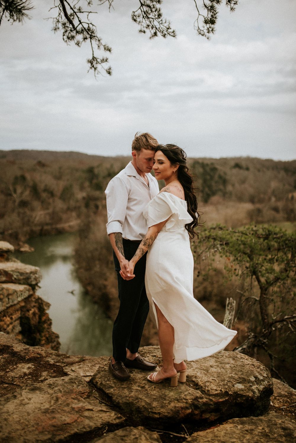 Bride and groom standing near the cliff with the view of the river below on an adventure elopement while affordable photographer takes photo