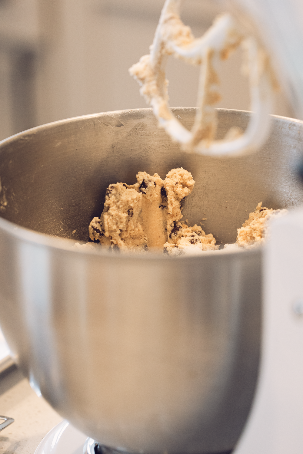 Close-up of cookie dough being mixed in a stainless steel stand mixer bowl.