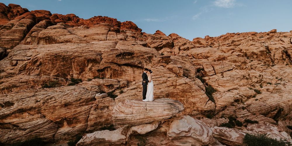 Bride and groom sharing romantic moment atop red sandstone rocks in desert canyon landscape.