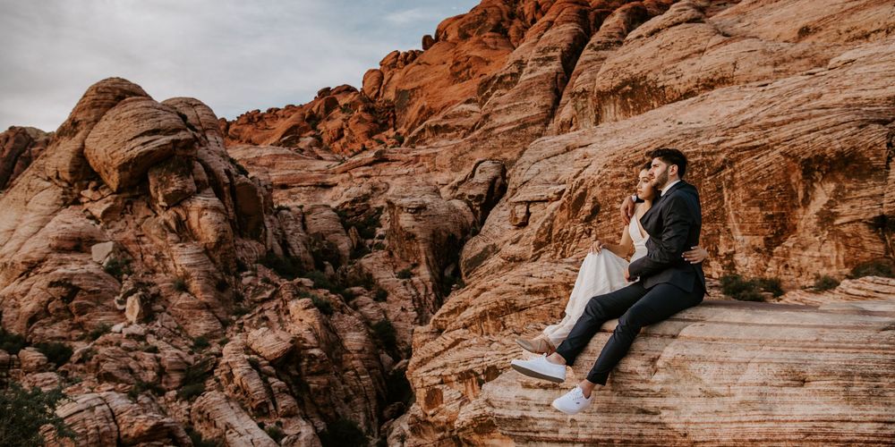 Newlyweds sitting together on wooden steps surrounded by stunning red rock canyon formations.