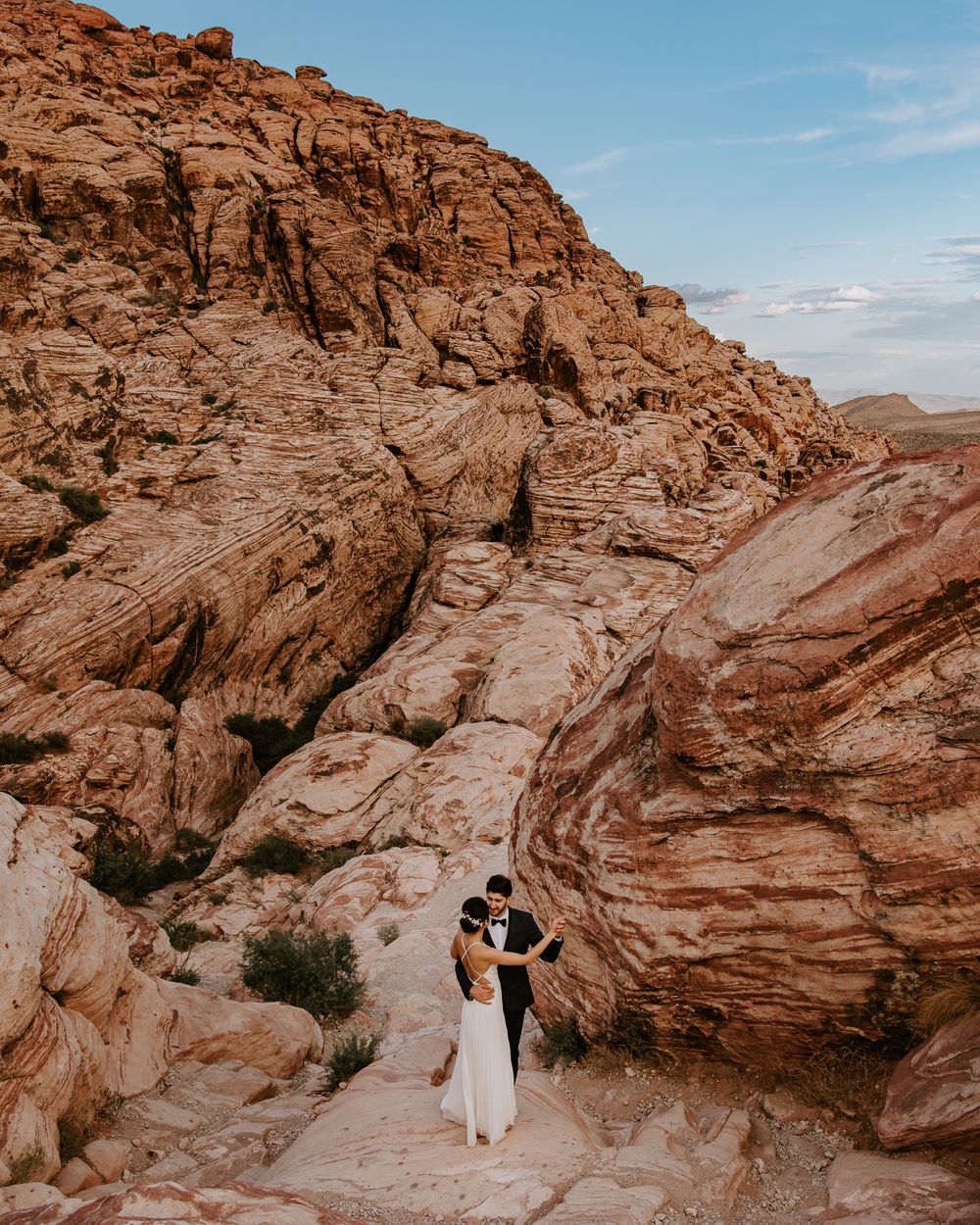 Wedding couple embracing on desert trail surrounded by dramatic red rock canyon walls.