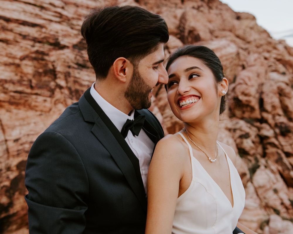 Smiling bride and groom sharing intimate moment with red rock canyon in background.