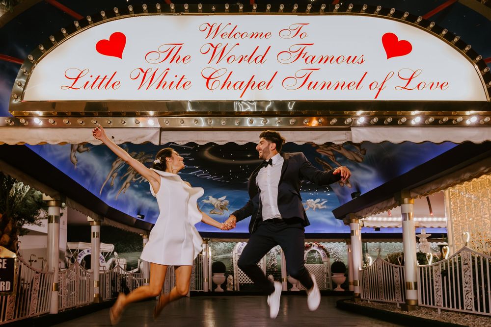 Couple jumping joyfully in front of the Little White Chapel Tunnel of Love sign in Las Vegas.