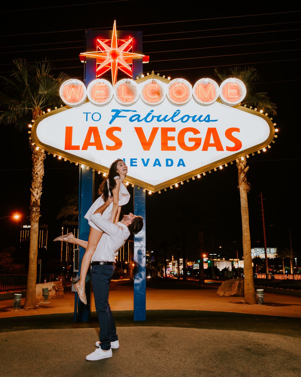 Couple celebrating under the iconic Welcome to Fabulous Las Vegas Nevada sign at night.