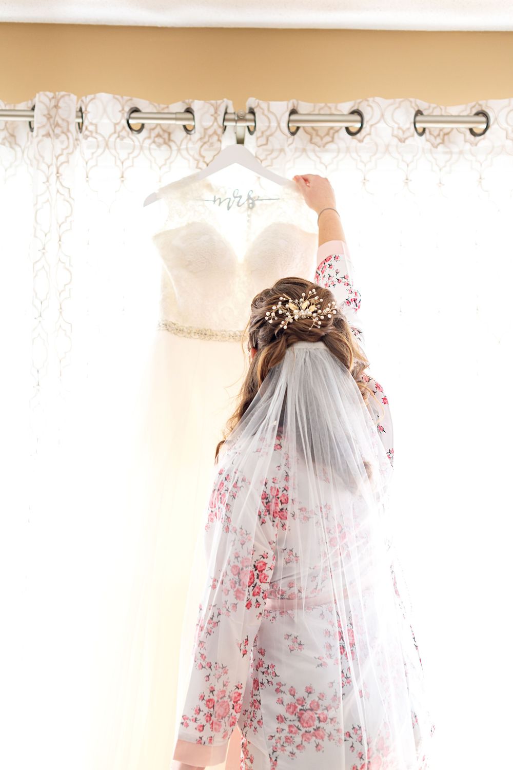 White wedding dresses with veils displayed on decorative curtain rods against a floral wallpapered wall.