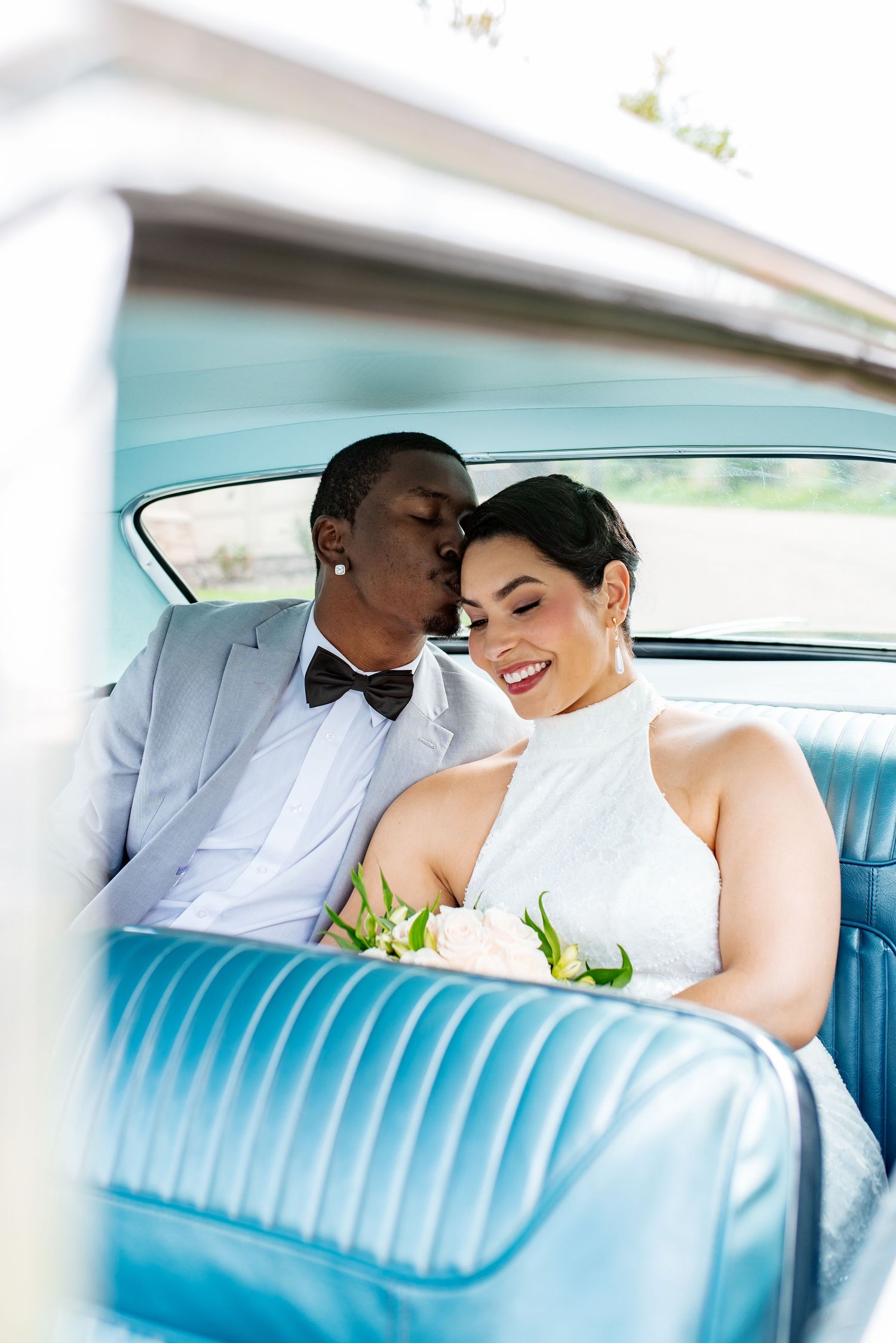 A romantic couple shares an intimate moment in the backseat of a classic car with turquoise blue leather seats.