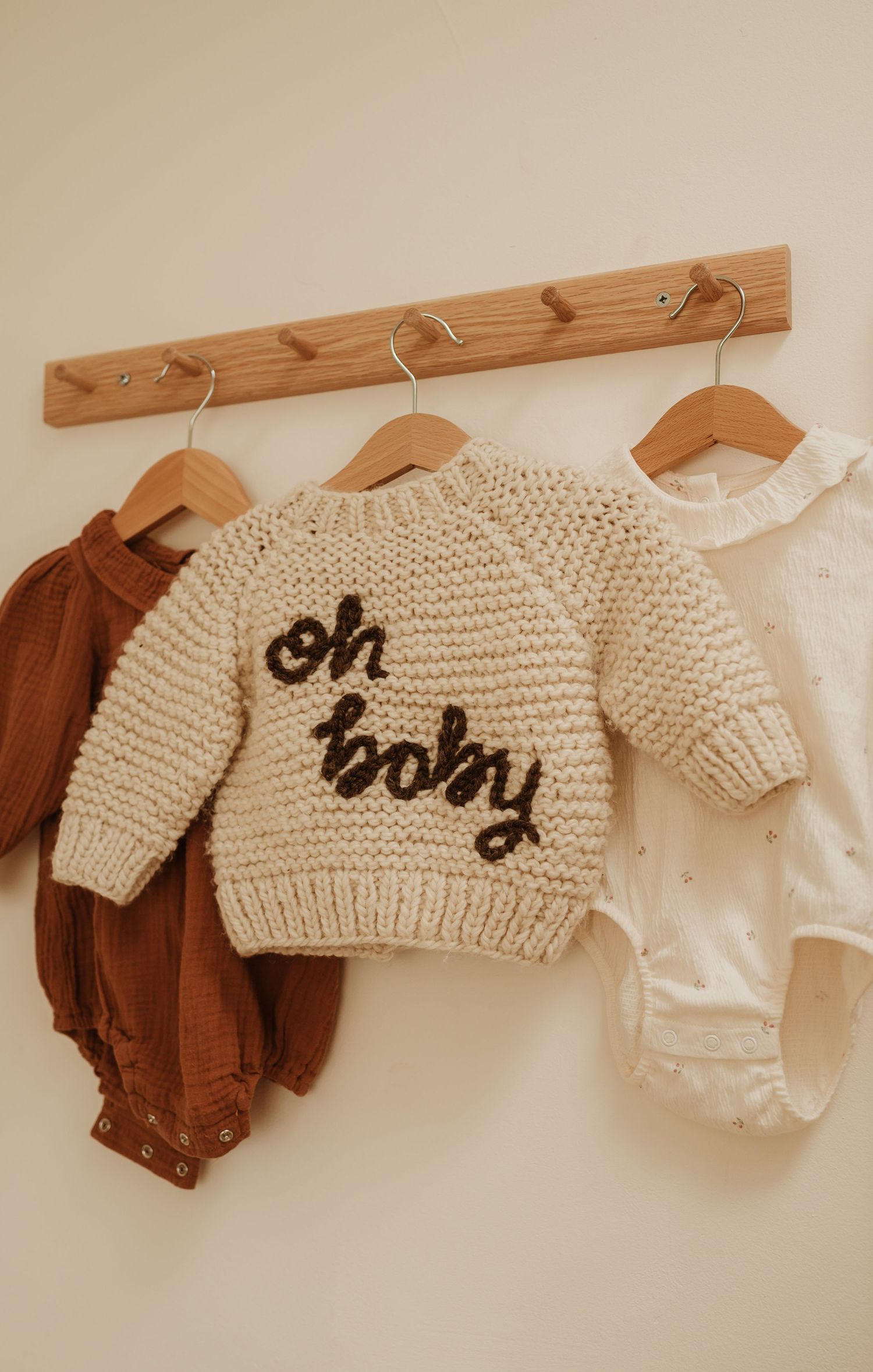 Organized closet featuring white, beige and coral clothing on wooden hangers with baby items on shelves.