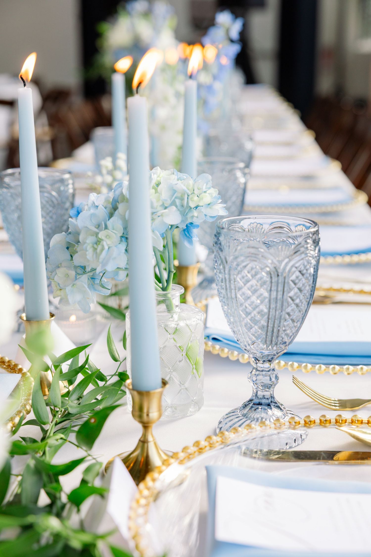 Elegant wedding table setting with pale blue candles, crystal glasses, and delicate floral arrangements on white linens.