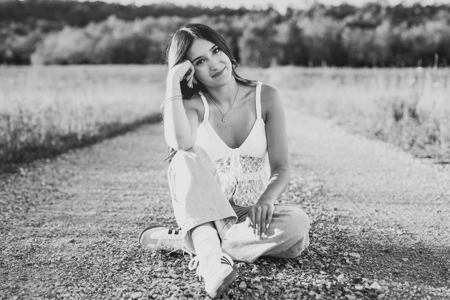 Black and white portrait of outdoor senior photo session, girl sitting in a field with a white shirt and jeans